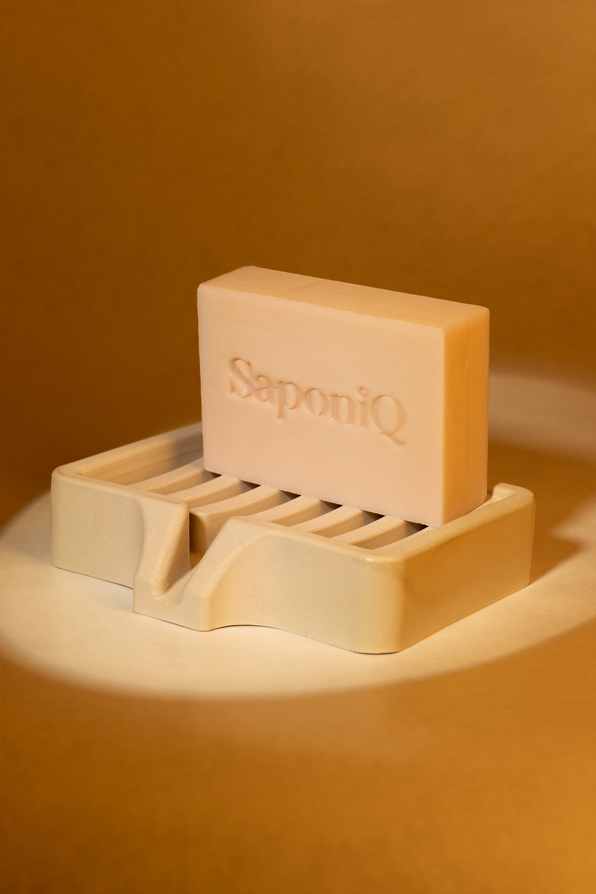 Bar of soap on a holder with 'SaponiQ' branding against a warm brown background