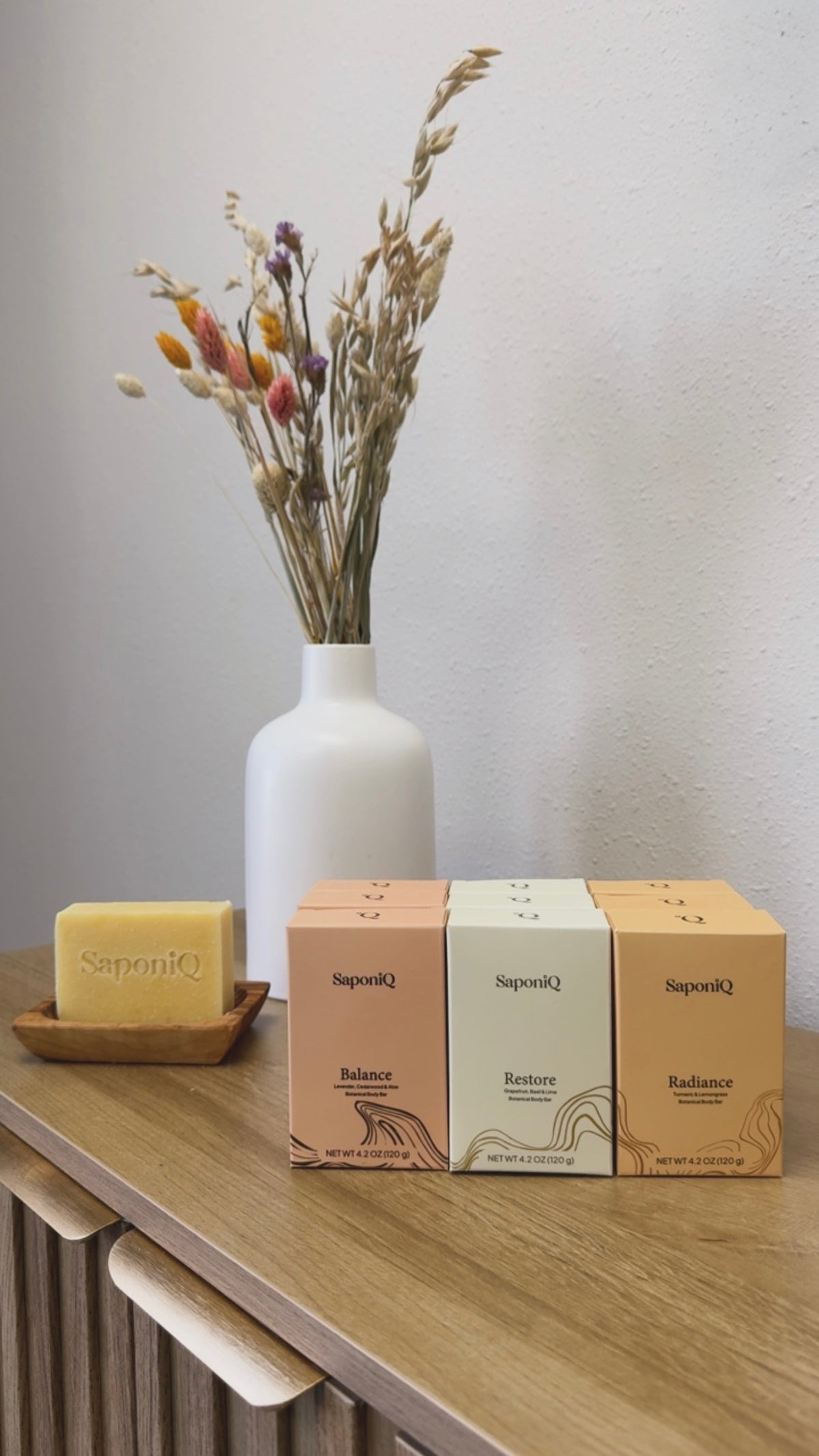 Balance, Restore, Radiance bar soaps in boxes and Radiance Bar Soap on a soap dish with a flower arrangement