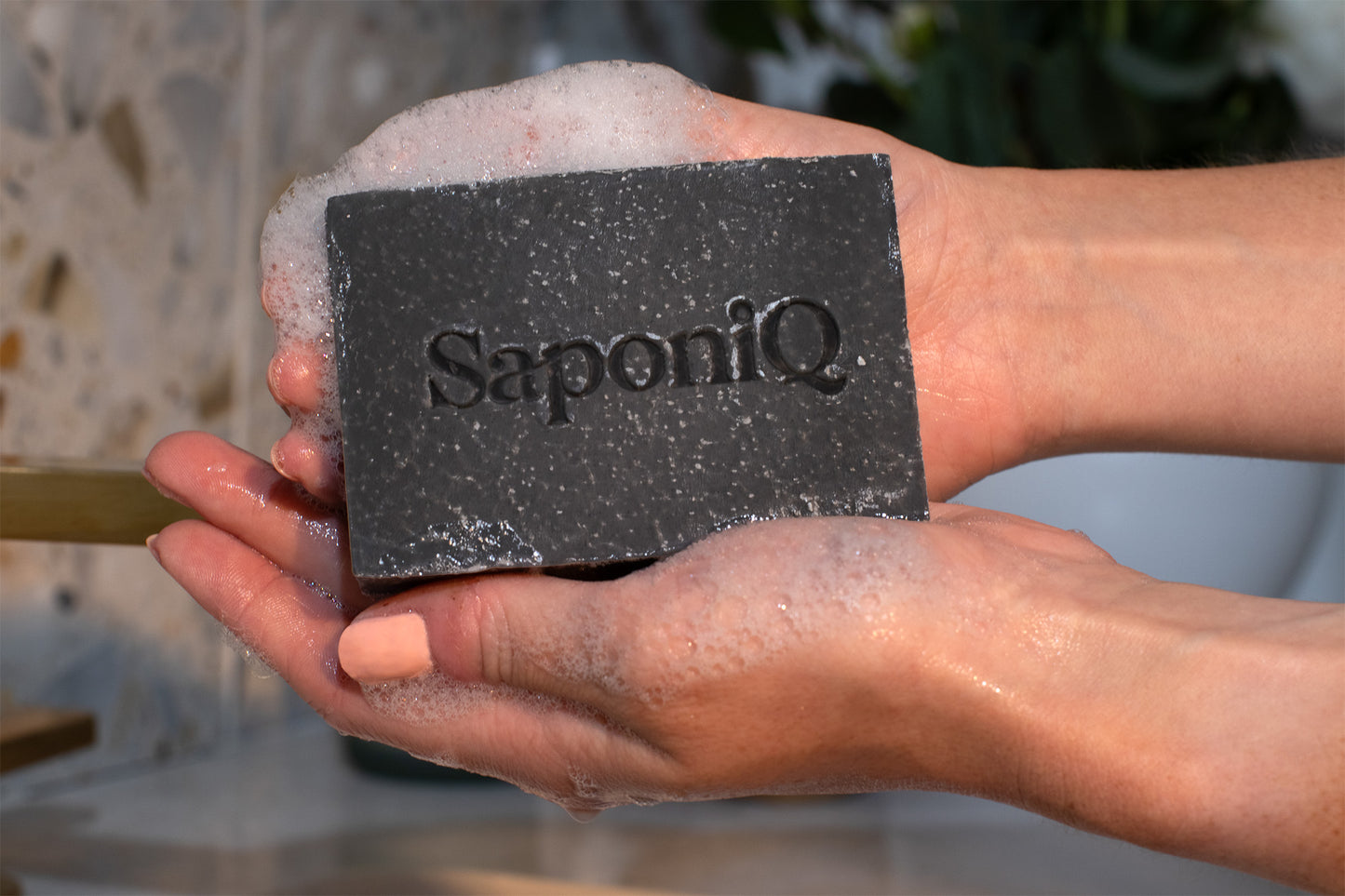 Person holding a bar of soap with 'SaponiQ' branding.