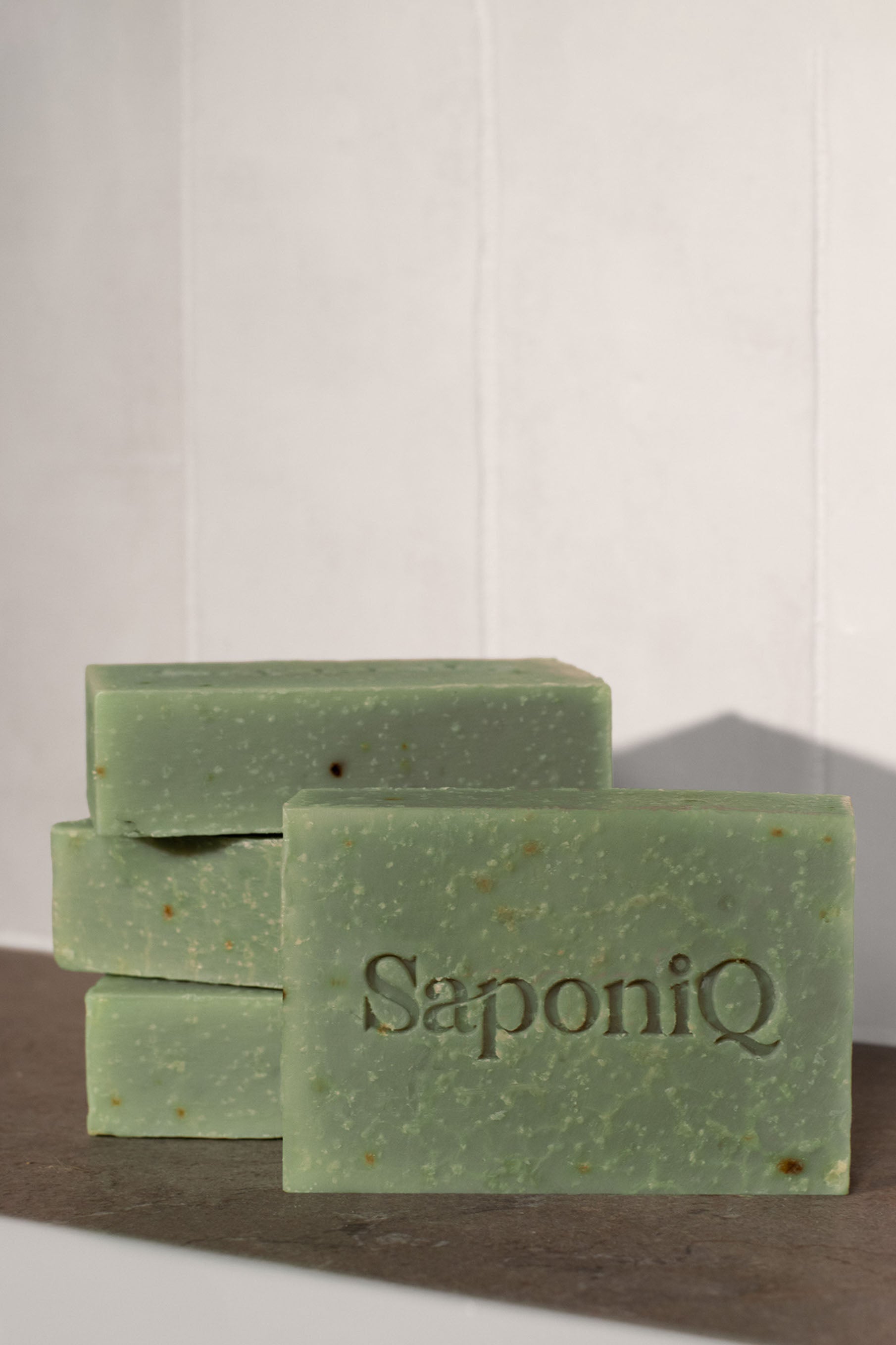 Green soap bars with 'SaponiQ' branding on a marble surface.