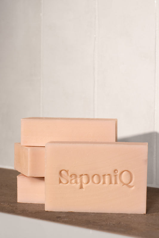 Rose colored bars of soap stacked on a wooden surface with 'SaponiQ' branding.