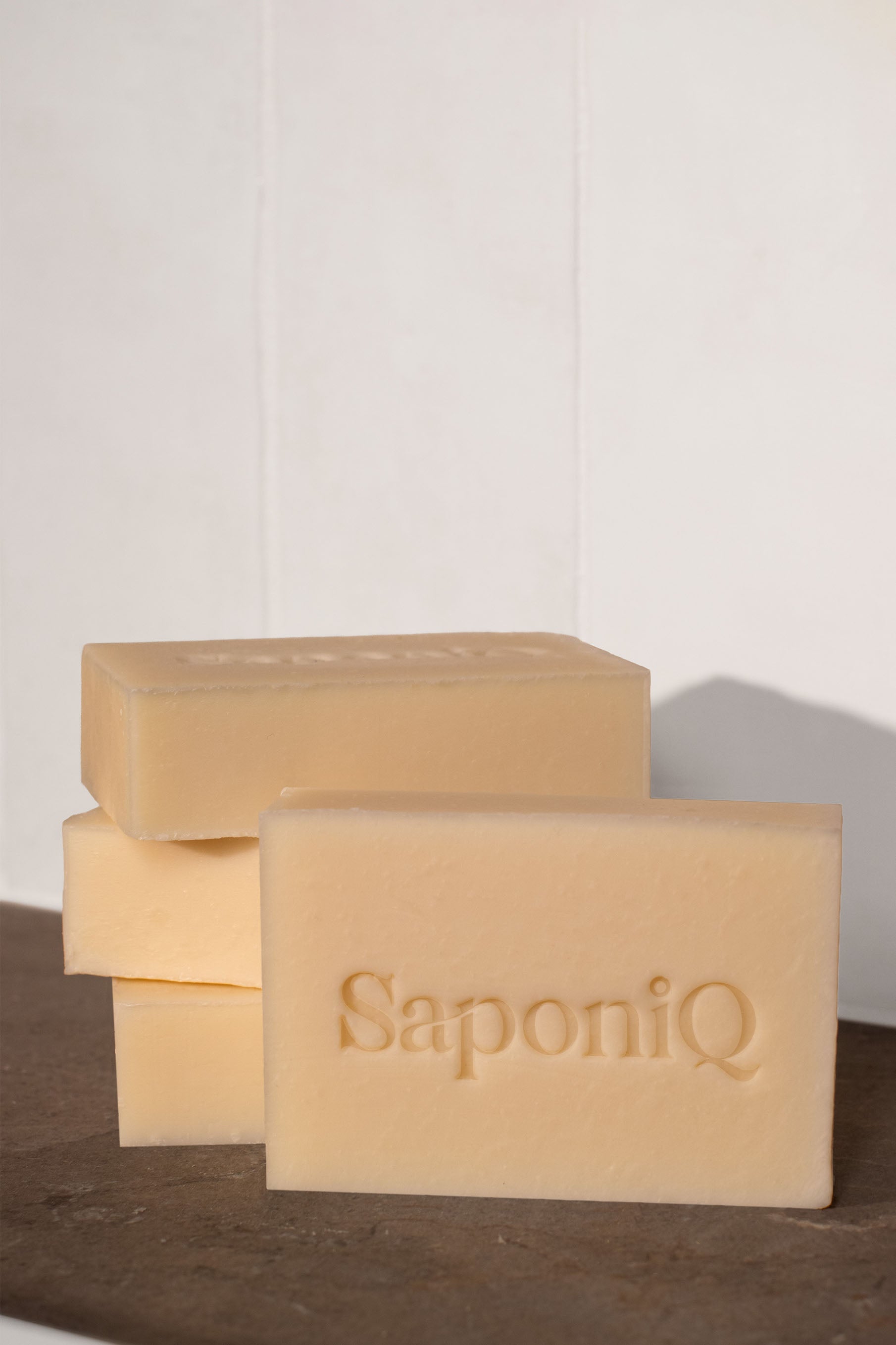 Off white colored bars of SaponiQ soap stacked on a marble surface with a white background