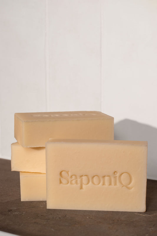 Off white colored bars of SaponiQ soap stacked on a marble surface with a white background