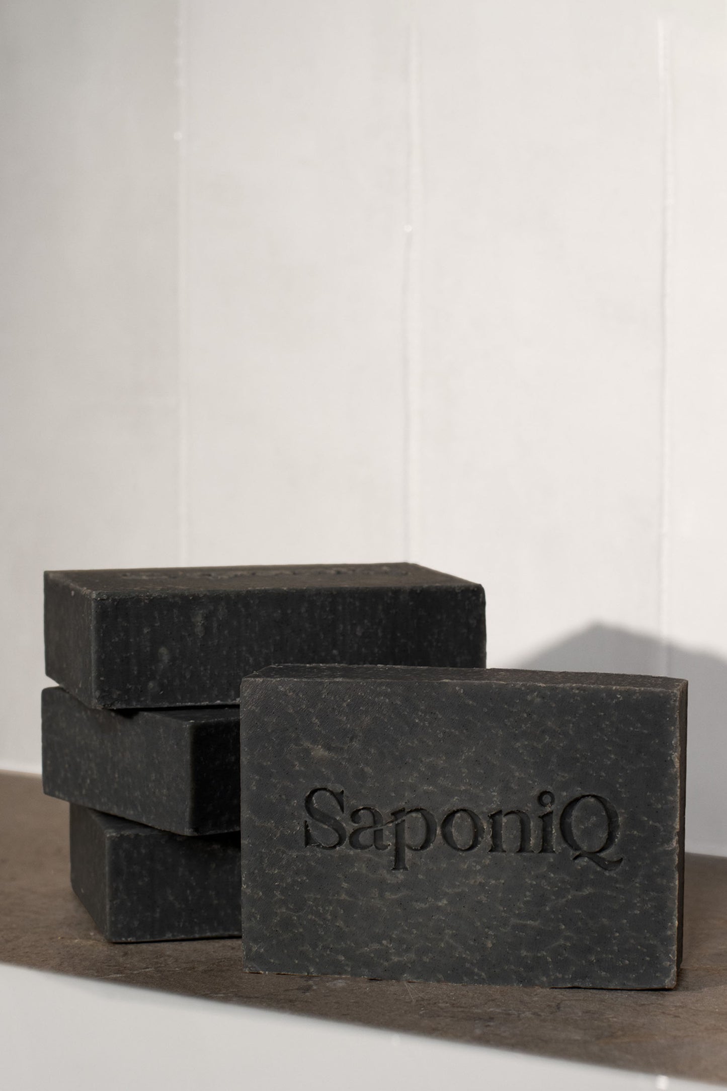 Three bars of black soap with 'SaponiQ' branding on a white background