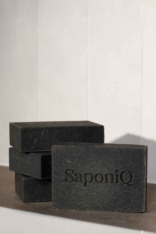 Three bars of black soap with 'SaponiQ' branding on a white background
