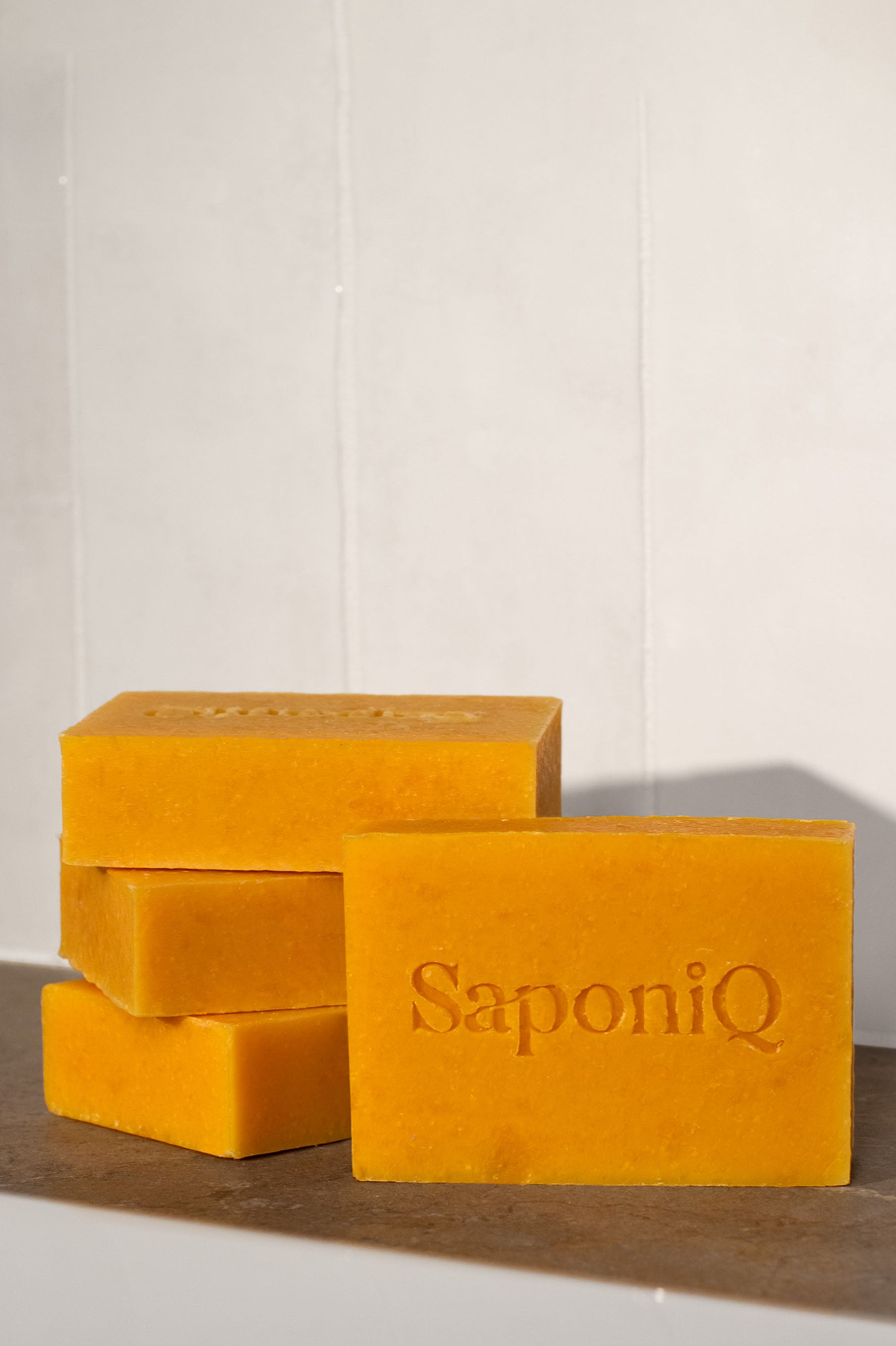 Bars of orange soap with 'SaponiQ' branding on a white background