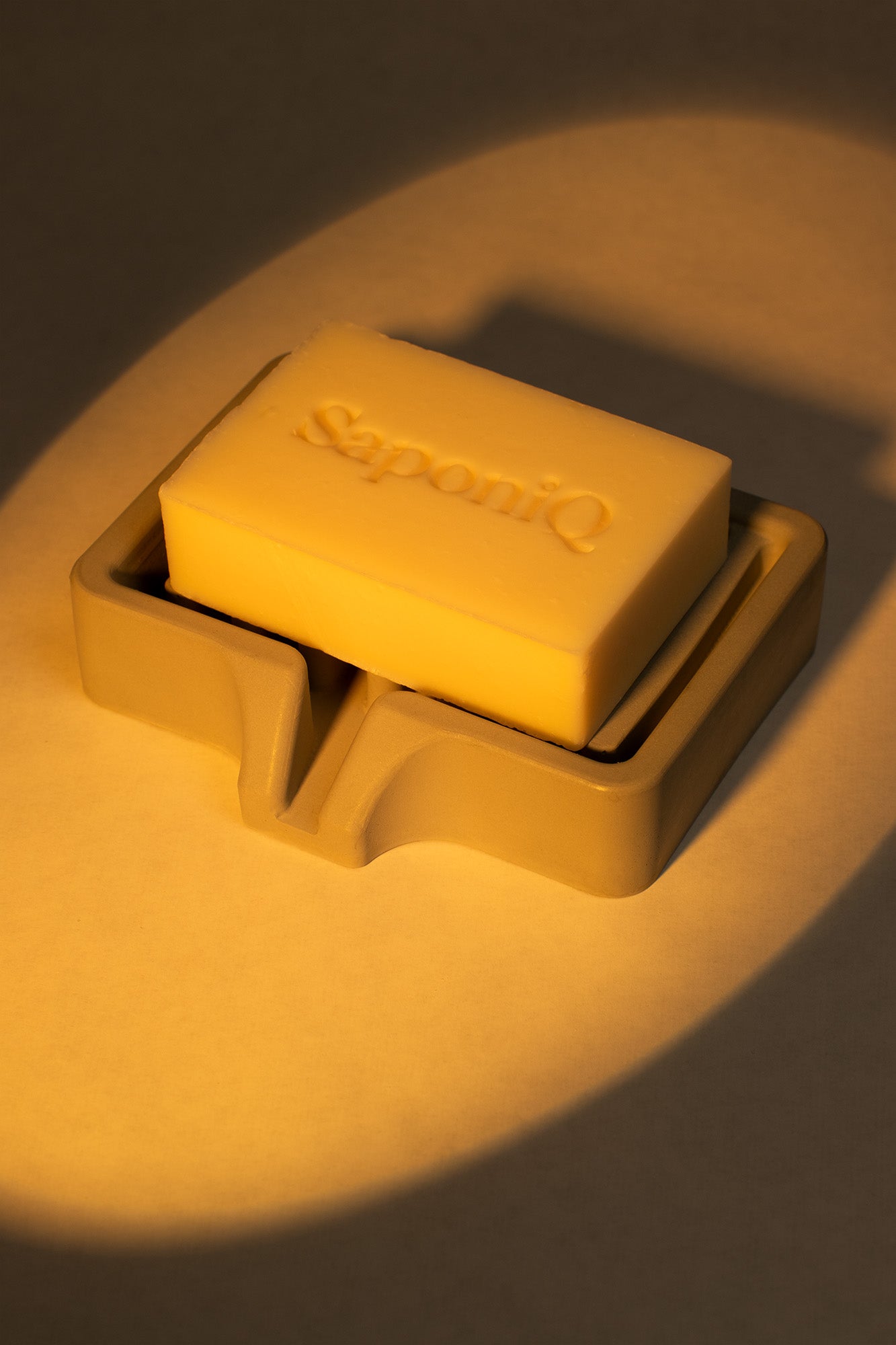 Bar of soap in a soap dish with 'SaponiQ' branding on a dark background