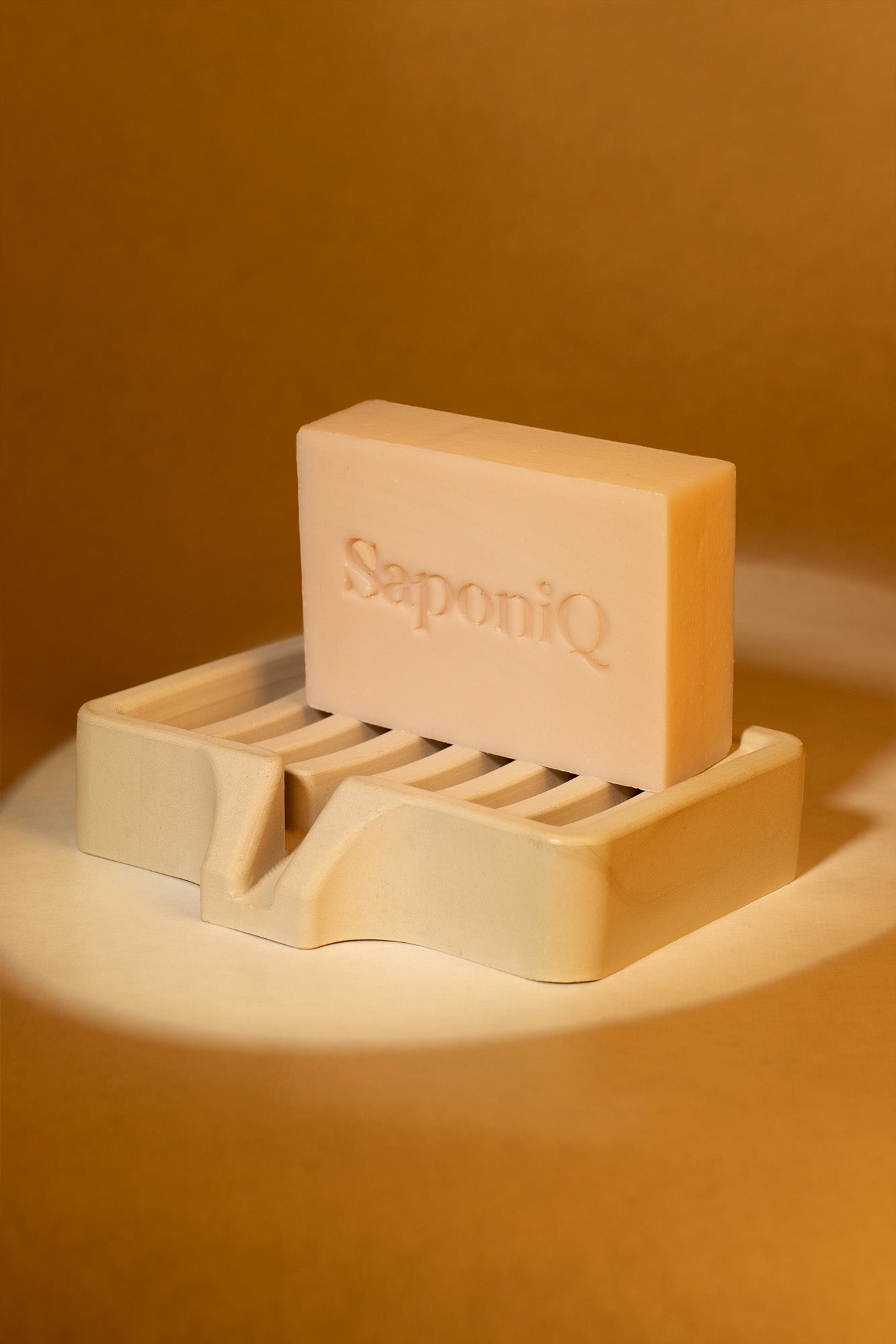 Bar of soap on a holder with 'SaponiQ' branding against a warm brown background
